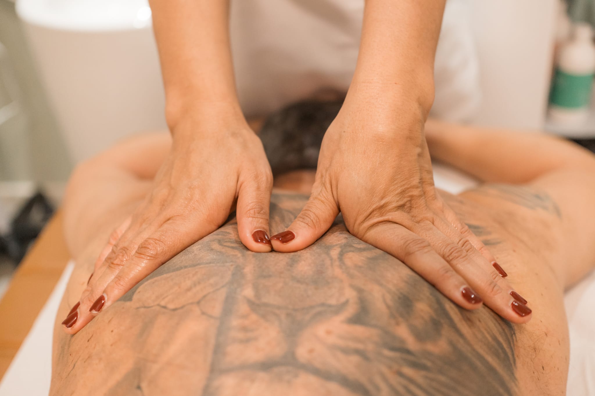 Close-up of hands pressing on a tattooed person’s back during a treatment, photographed in warm indoor lighting.